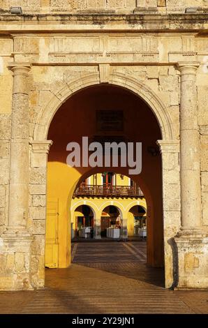 Vue à travers les arches du portail au bâtiment historique jaune avec balcons et arches de porte dans la lumière chaude et l'ombre, Carthagène, Colombie, UNESCO World H Banque D'Images