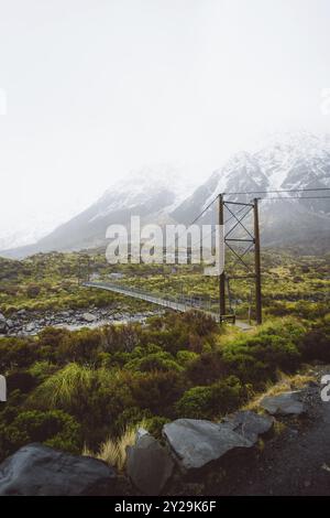 Pont suspendu dans un paysage montagneux avec des prairies et des rochers sous un ciel nuageux, Hooker Valley Track, Nouvelle-Zélande, Océanie Banque D'Images