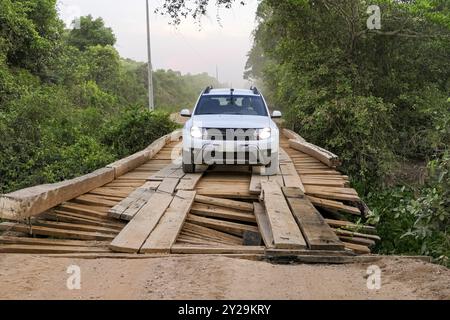 SUV blanc traversant un pont en bois délabré sur la route de Transpantaneira à travers le nord du Pantanal par un matin brumeux, Mato Grosso, Brésil, South Amer Banque D'Images