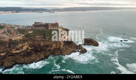 Vue aérienne d'un vieux phare sur une falaise avec une forteresse sur la côte de l'océan Atlantique dans la ville de Nazare, Portugal. Banque D'Images