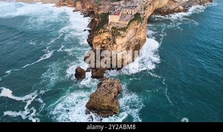 Vue aérienne d'un vieux phare sur une falaise avec une forteresse sur la côte de l'océan Atlantique dans la ville de Nazare, Portugal. Banque D'Images