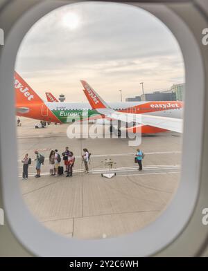 Des gens faisant la queue pour embarquer sur un vol Easyjet sur la piste photographiée depuis la fenêtre du hublot de cabine Banque D'Images
