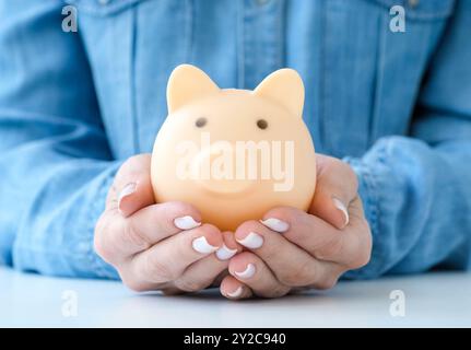 Femme dans une chemise bleue tenant tirelire sur une table blanche. Concept d'économie d'argent. Banque D'Images
