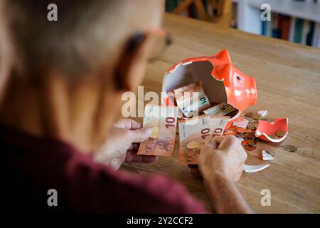 Berlin, Deutschland. 05th Sep, 2024. Photo symbolique sur le thème des finances dans la vieillesse - la pauvreté de la vieillesse. Un vieil homme est assis à la maison à la table devant une tirelire cassée et compte l'argent. Berlin, le 5 septembre 2024. Crédit : dpa/Alamy Live News Banque D'Images