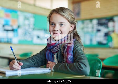 Fille, portrait et écriture avec livre en classe pour sourire, notes et excité par l'éducation. Enfant, cahier et fierté avec info, bourse ou Banque D'Images