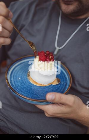 Gros plan de délicieuse tarte. Gros plan de l'homme caucasien mangeant un dessert avec un tourbillon de meringue et des baies dans un café Banque D'Images