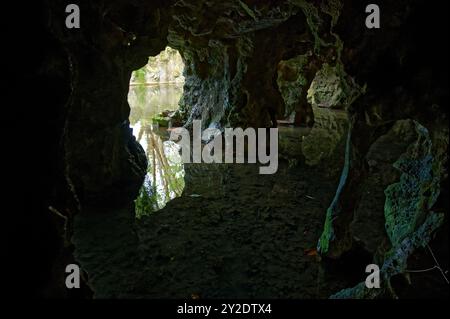 Vue depuis une ouverture de grotte faiblement éclairée, donnant sur une surface d'eau tranquille et réfléchissante Banque D'Images