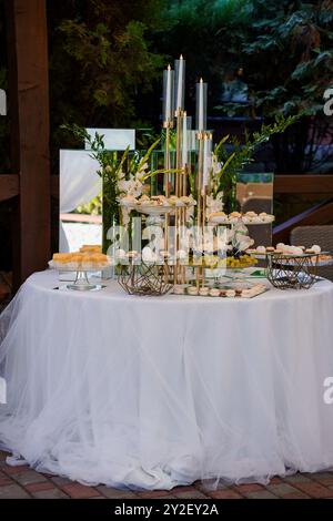 Élégante table de desserts pour événement extérieur avec bougies et décorations florales. Banque D'Images