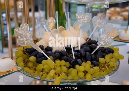 Présentoir de desserts élégant avec des pop en forme de cœur et un arrangement de fruits éclatant. Banque D'Images