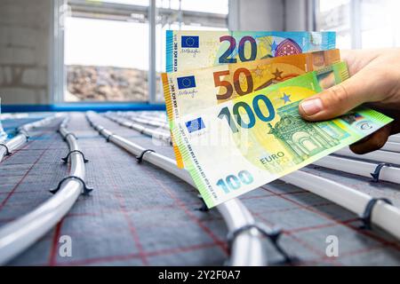 Main tenant les billets de banque en euros devant les tuyaux pour le chauffage par le sol hydronique Banque D'Images