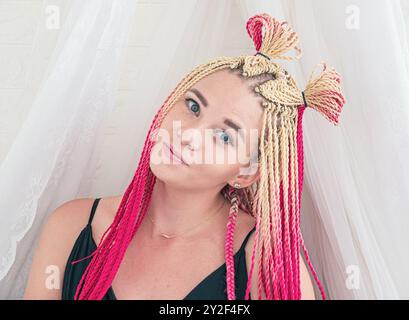 Jeune femme avec une coiffure tressée bicolore tendance aux couleurs rose et blonde, posée sur un fond blanc doux Banque D'Images