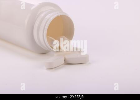 Un gros plan d'un flacon de pilule blanc renversant des comprimés, illustrant parfaitement les concepts de soins de santé, de médicaments et de traitement médical professionnel Banque D'Images