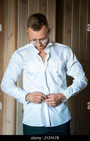 Élégante chemise de robe blanche Crisp Buttoning Gentleman dans un intérieur en bois élégant. Banque D'Images