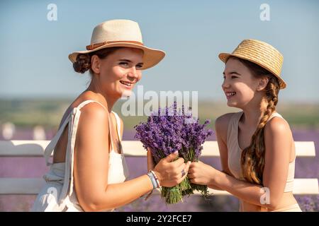 Une femme et un enfant sont assis sur un banc dans un champ de fleurs violettes lavande. La femme tient un bouquet de fleurs et l'enfant tient un Banque D'Images