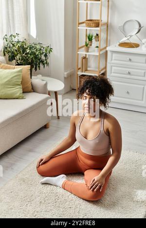 Une jeune femme est assise paisiblement sur un tapis mou, perdue dans ses pensées à la maison. Banque D'Images