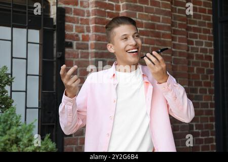 Jeune homme enregistrant des messages vocaux via smartphone à l'extérieur Banque D'Images