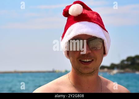 27 août 2024 : un homme avec un chapeau de Noël et des lunettes de soleil sur la plage - image symbolique pour un voyage de longue distance dans les Caraïbes ou d'autres destinations de vacances ensoleillées pendant la saison de Noël *** Ein Mann mit Weihnachtsmütze und Sonnenbrille am Strand Symbolbild für eine Fernreise in die Karibik oder andere sonnige Urlaubsziele während der Weihnachtszeit Banque D'Images