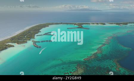 Bateaux naviguant sur le lagon turquoise de l'île de Polynésie française avec bungalows sur l'eau, paradis tropical à Bora Bora. Complexe de vacances de luxe dans la baie océanique de récif de corail. Vol avec vue aérienne par drone Banque D'Images