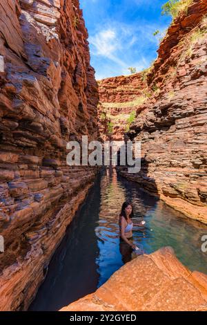 Une aventurière femme traverse l'étroite gorge de Hancock, aux parois escarpées et remplies d'eau, dans le magnifique parc national de Karijini en Australie. Banque D'Images