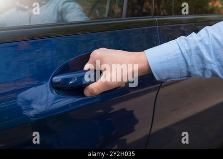 La main de l'homme ouvre une porte avant de la voiture bleue Banque D'Images