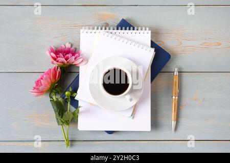 Composition artistique avec bloc-notes vierge ouvert et stylo, tasse de café noir, fleur de dahlias rose sur table en bois bleu. Concept de bureau festif. Tasse de café du matin. Banque D'Images