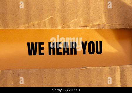 Nous vous entendons un message écrit sur du papier en carton déchiré déchiré avec un fond orange. Conceptuel nous entendons vous symbole. Copier l'espace. Banque D'Images