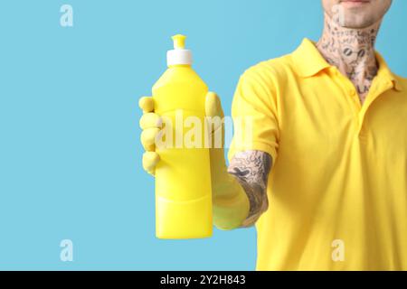 Jeune homme tatoué avec bouteille de détergent sur fond bleu, gros plan Banque D'Images