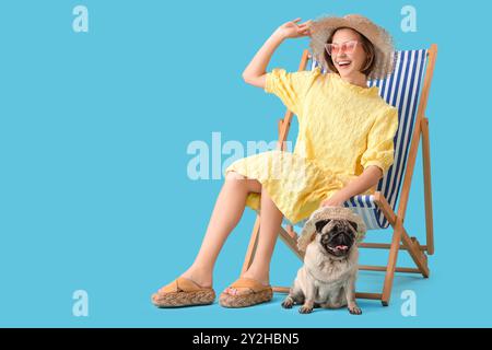 Jeune femme avec chien de pug mignon assis sur une chaise longue sur fond bleu Banque D'Images