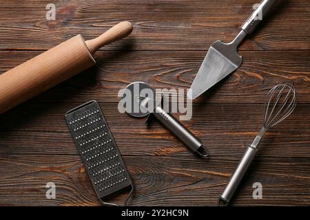 Ensemble de différents ustensiles de cuisine avec coupe-pizza en acier inoxydable sur fond en bois Banque D'Images