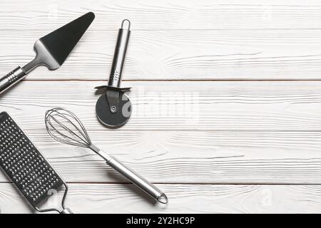 Ensemble d'ustensiles de cuisine en acier inoxydable avec coupe-pizza sur fond en bois blanc Banque D'Images