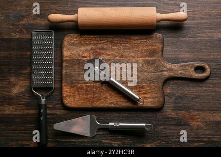 Ensemble de différents ustensiles de cuisine avec coupe-pizza en acier inoxydable sur fond de bois foncé Banque D'Images