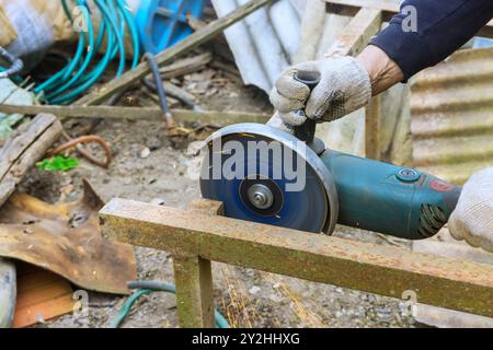 À l'aide d'une scie à main de meuleuse d'angle, l'ouvrier coupe des cadres métalliques Banque D'Images