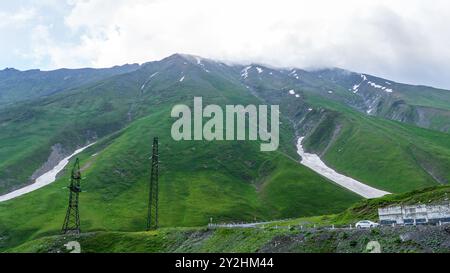 Vue panoramique depuis la colline herbeuse sur les montagnes Kazbek et la vallée verdoyante traversée de routes Banque D'Images