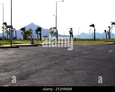 Les palmiers balancent doucement dans la brise près du parking de l'aéroport de Sharm El Sheikh. Le paysage présente des montagnes lointaines sous un ciel lumineux, cr Banque D'Images