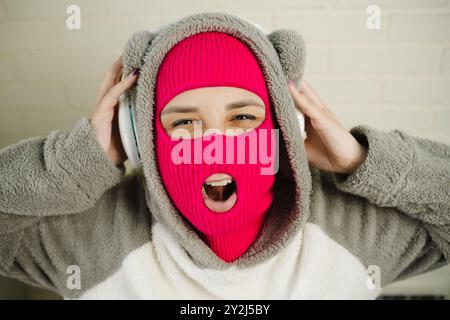 Femme en Balaclava rose dansant contre un mur de briques blanches Banque D'Images