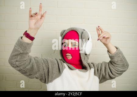 Femme en Balaclava rose dansant contre un mur de briques blanches Banque D'Images