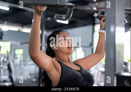 Une image en gros plan d'une femme asiatique forte et sportive en vêtements de sport s'exerce aux barres de traction dans le gymnase, entraînant ses épaules et ses bras. entraînement, Banque D'Images