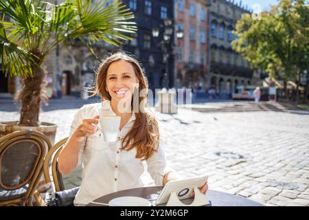 Jeune femme appréciant le café dans un charmant café au coeur d'une place historique de la ville. Banque D'Images