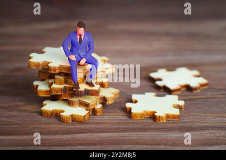 Figurine d'homme d'affaires miniature perchée sur des pièces de puzzle empilées sur une surface en bois, symbolisant la résolution de problèmes et la prise de décision. Banque D'Images