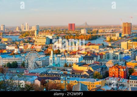 Kiev, Ukraine - 14 octobre 2023 : vue détaillée du district de Podil à Kiev avec une grande roue et une ligne d'horizon moderne éclairée par la lumière du soleil d'automne. Banque D'Images