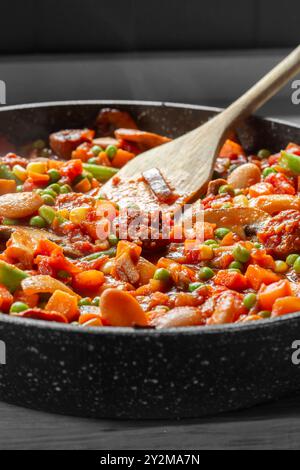 Chorizo espagnol, haricots rouges, ragoût de tomates et légumes avec champignons et oignons. Dans une poêle sur une planche à découper en bois. Banque D'Images