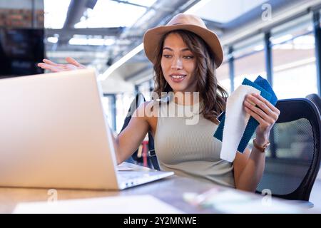 Tenant des échantillons de tissu, femme discutant des idées de design d'intérieur sur ordinateur portable dans le bureau Banque D'Images