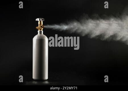 Une bouteille de gaz CO2 avec une vanne ouverte et du gaz s'échappant vers l'extérieur sur un fond noir. Banque D'Images