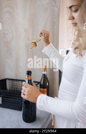 La jeune femelle ouvre une bouteille de champagne. Fille aux cheveux bouclés préparant un cocktail Banque D'Images