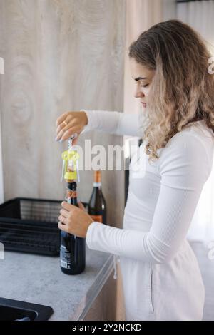 La jeune femelle ouvre une bouteille de champagne. Fille aux cheveux bouclés préparant un cocktail Banque D'Images