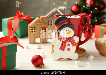 Délicieux cookie en forme de bonhomme de neige, tasse avec cacao et décor de Noël sur table en bois blanc Banque D'Images