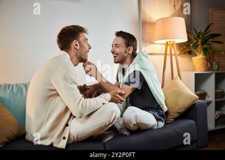 Deux hommes partagent un moment sincère rempli de rire et d'amour dans leur salon confortable. Banque D'Images