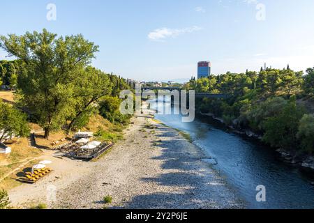 La rivière Morača qui traverse le centre-ville de Podgorica au Monténégro dans les Balkans par une journée d'été ensoleillée avec un ciel bleu, avec une petite plage et un bar. Banque D'Images