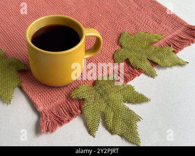Automne, tasse à café jaune et textile orange, et feuilles d'automne vertes Banque D'Images