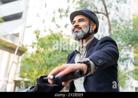 D'en bas, un Indien, habillé en homme d'affaires, regarde loin en faisant du vélo électrique dans une rue de la ville. Banque D'Images